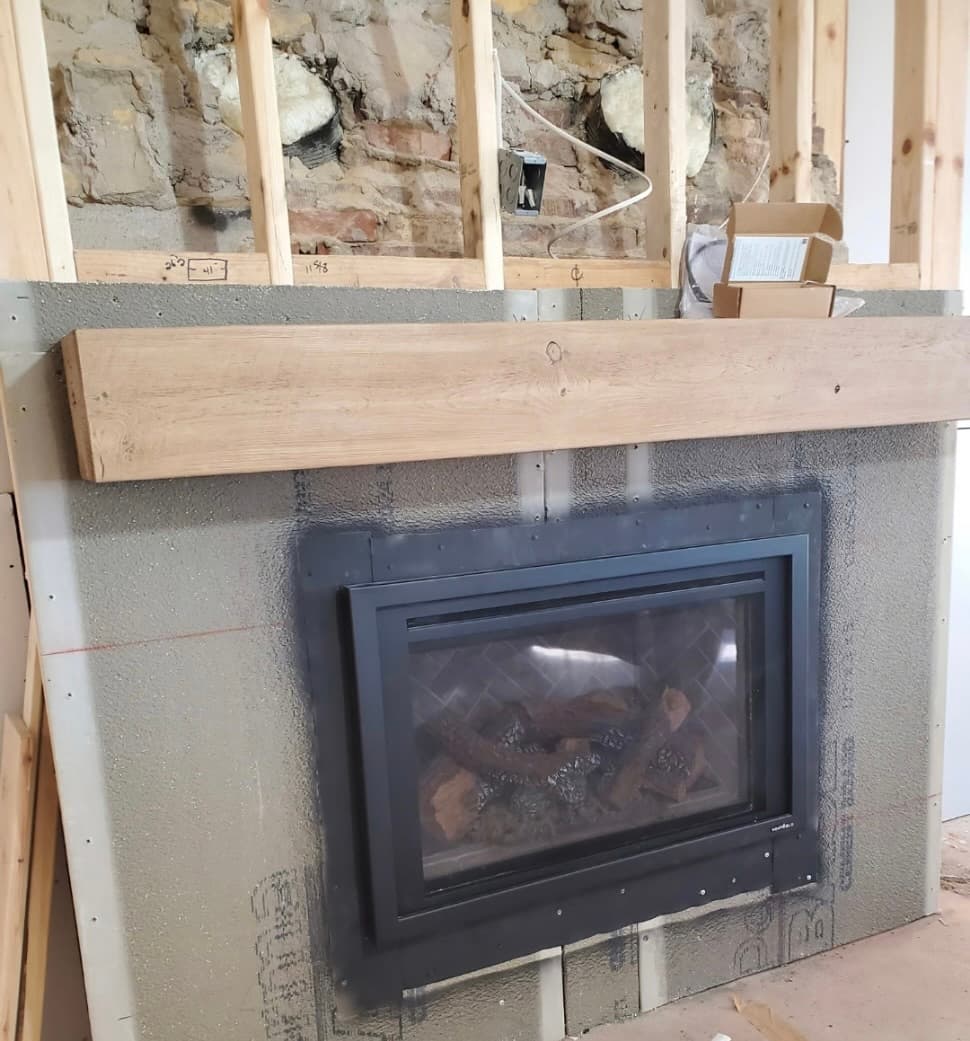 Gas fireplace mid-install with a rustic wood beam mantel and framed-out wall behind