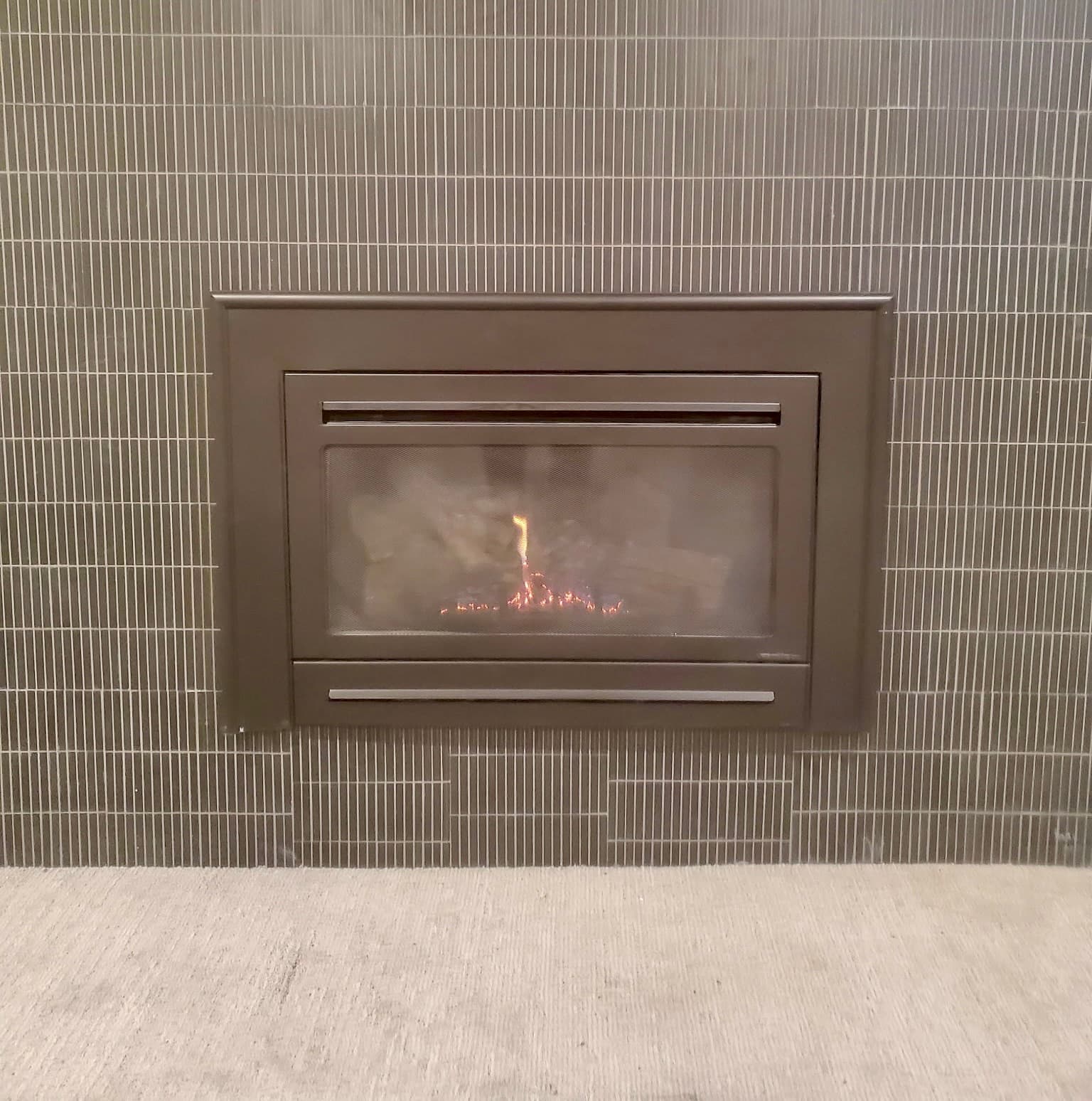 Gas insert surrounded by gray vertical linear tile with a small flame burning