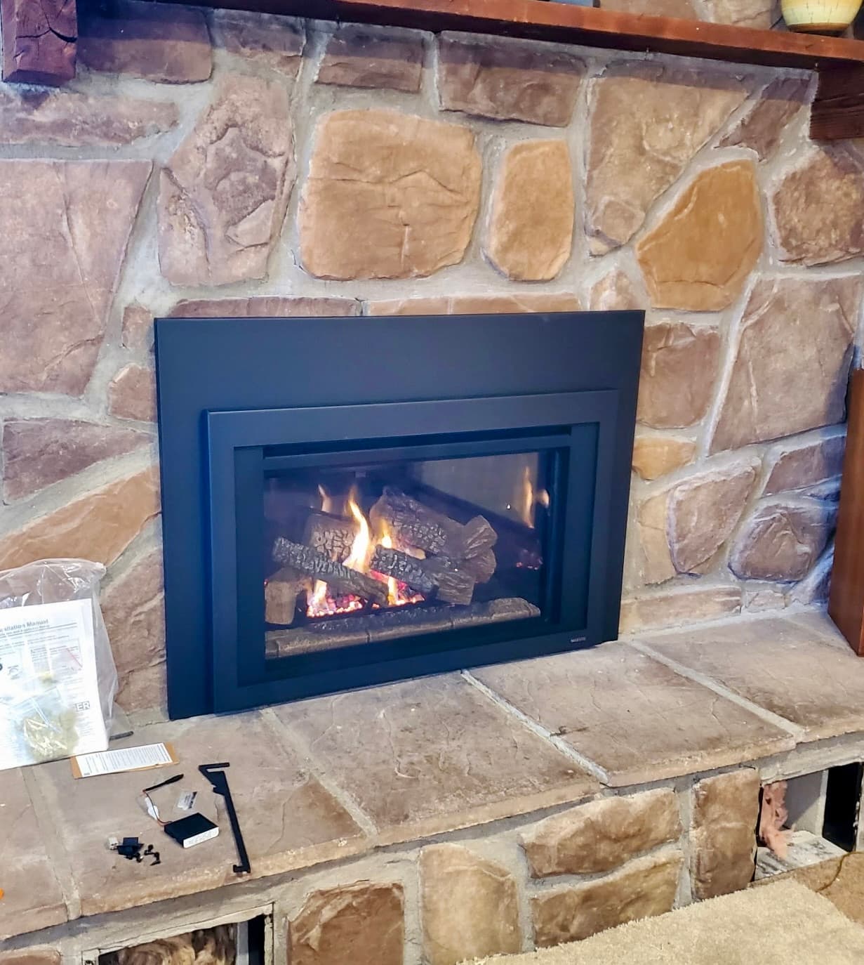 Black gas insert installed in a natural fieldstone fireplace with a stone hearth and burning logs