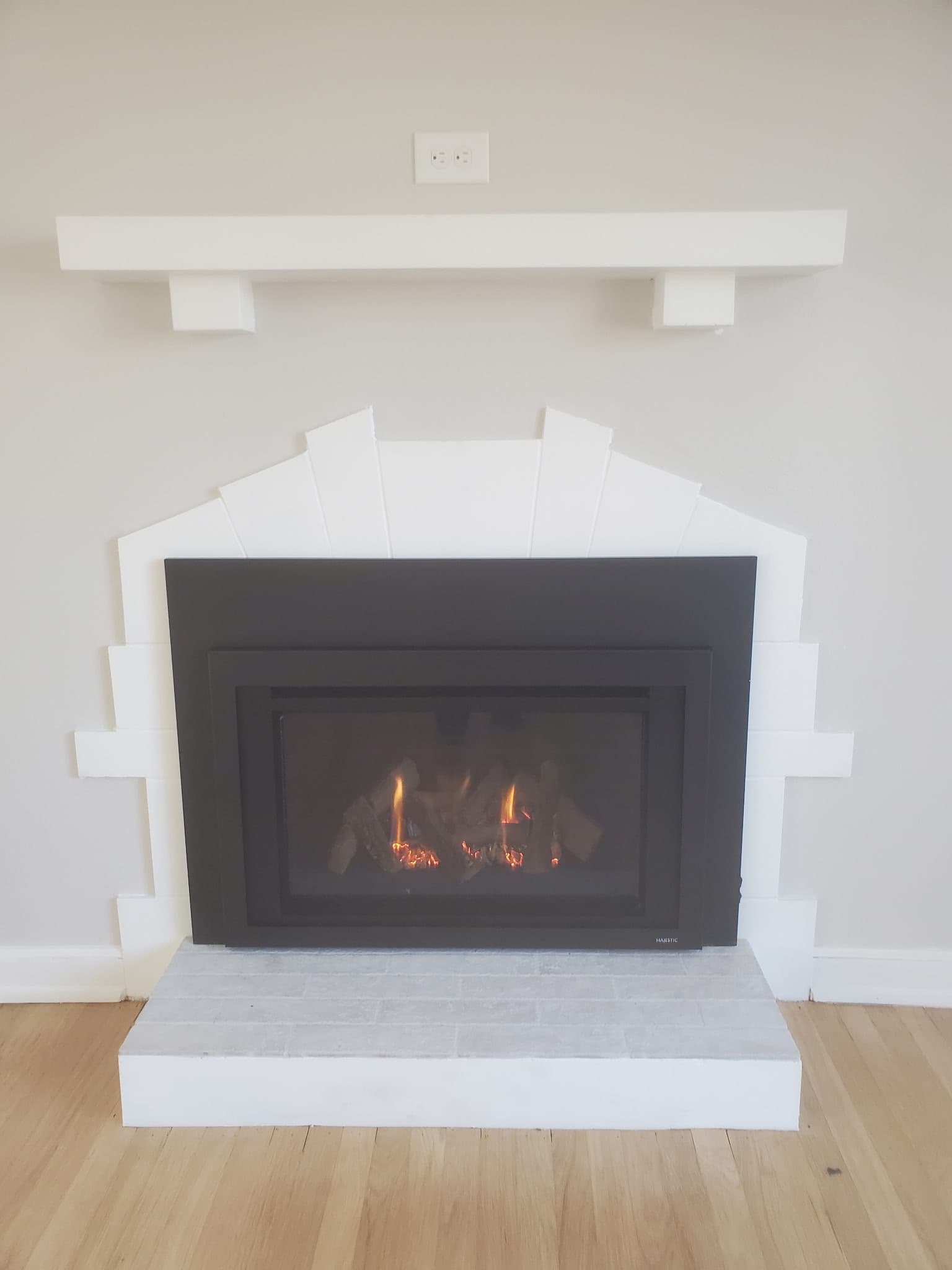 Modern gas insert framed by a stepped white surround and floating mantel with a tiled hearth