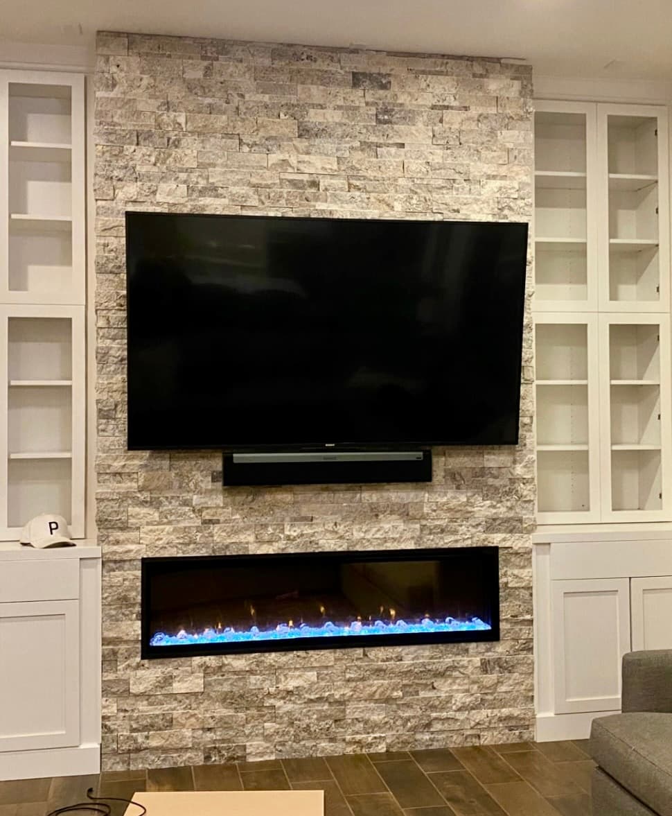 Linear fireplace and mounted TV on a stacked stone wall flanked by white glass-front built-in cabinets