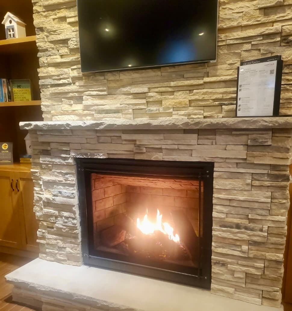 Gas fireplace set in a floor-to-ceiling stacked stone surround with a TV mounted above and a lit fire
