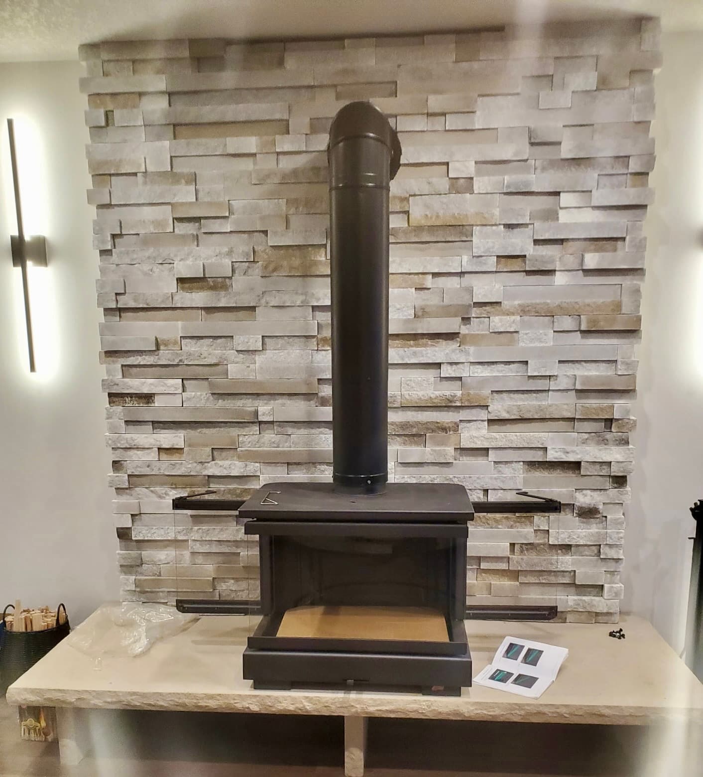 Black free-standing wood stove with stovepipe against a light stacked stone wall and stone hearth